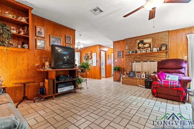 living room featuring ceiling fan with notable chandelier, a fireplace, and wooden walls