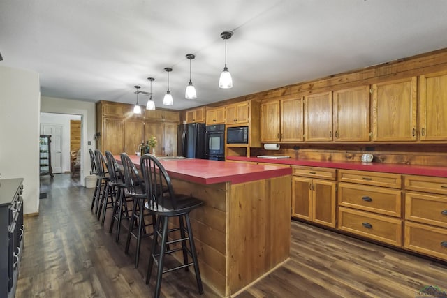 kitchen featuring dark wood-type flooring, hanging light fixtures, a kitchen bar, a kitchen island, and black appliances