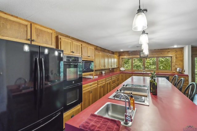 kitchen featuring sink, decorative light fixtures, wood walls, and black appliances