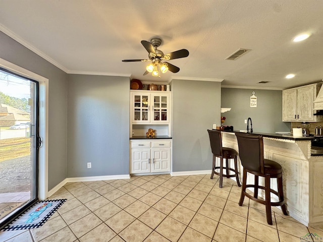 kitchen featuring white cabinets, light tile patterned floors, crown molding, and a breakfast bar area