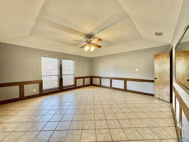 tiled empty room featuring ceiling fan and a tray ceiling