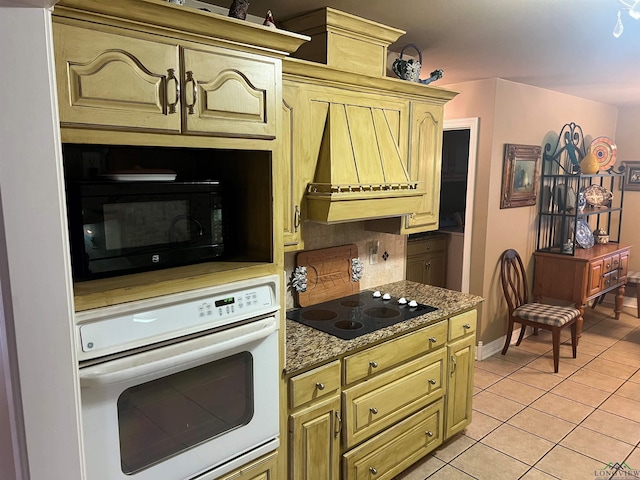 kitchen featuring tasteful backsplash, light tile patterned flooring, black appliances, premium range hood, and baseboards