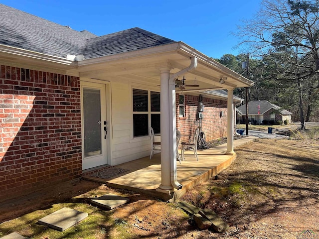 entrance to property featuring a shingled roof and brick siding