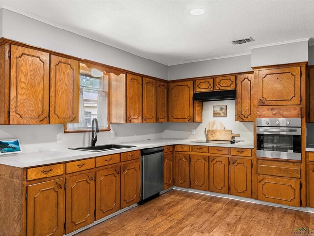 514 N St, Gilmer, TX 75644 - kitchen featuring stainless steel appliances, light countertops, brown cabinetry, light wood-style flooring, and under cabinet range hood