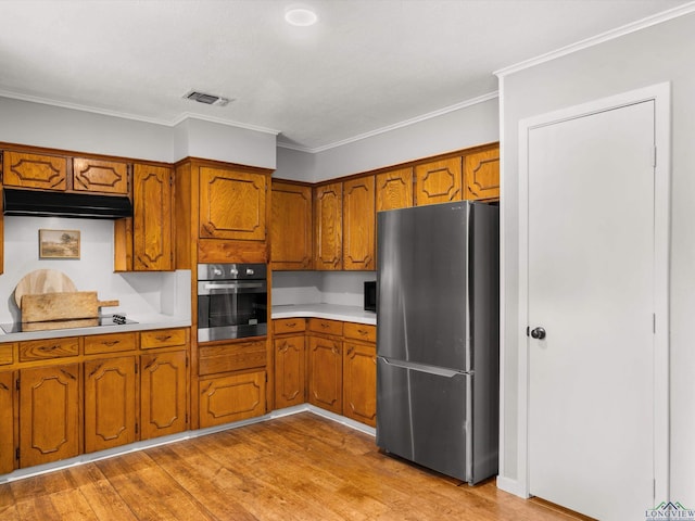 514 N St, Gilmer, TX 75644 - kitchen featuring appliances with stainless steel finishes, brown cabinets, light countertops, light wood-style floors, and crown molding