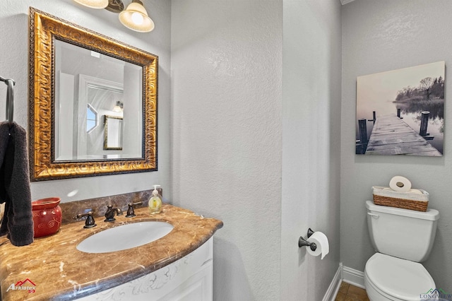 half bath featuring a textured wall, vanity, baseboards, and toilet