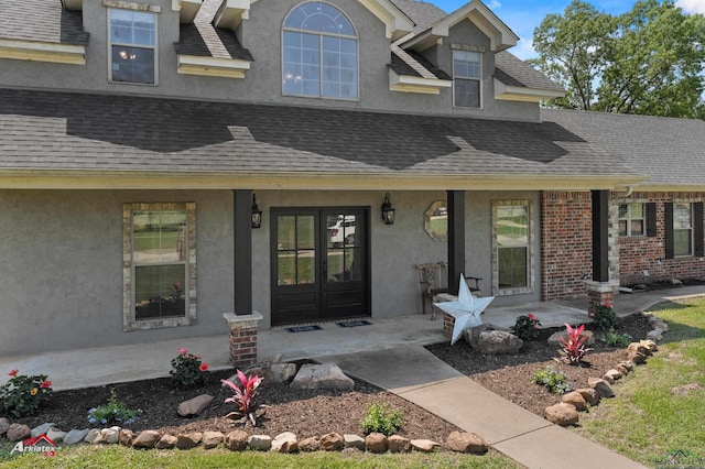doorway to property featuring a porch, roof with shingles, and stucco siding