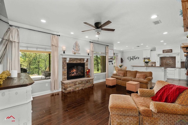 living room featuring crown molding, a fireplace, a ceiling fan, visible vents, and wood finished floors