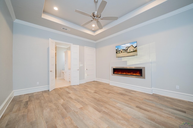 interior space with a warm lit fireplace, light wood-style flooring, baseboards, ornamental molding, and a tray ceiling