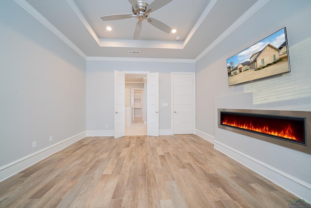 unfurnished living room featuring visible vents, baseboards, light wood-style floors, a lit fireplace, and a tray ceiling