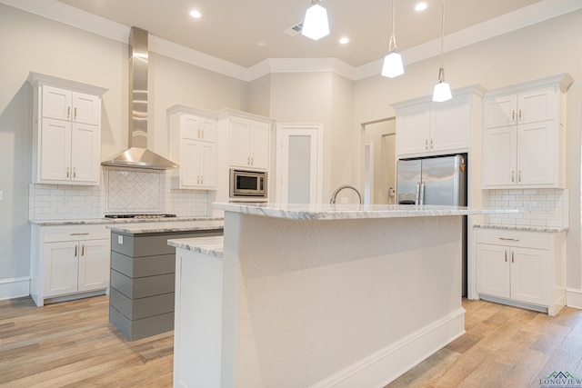 kitchen with a kitchen island with sink, wall chimney range hood, light wood finished floors, and appliances with stainless steel finishes