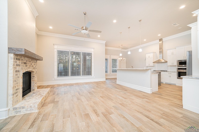 unfurnished living room with ceiling fan with notable chandelier, a fireplace, light wood-style flooring, and crown molding