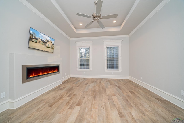 unfurnished living room featuring recessed lighting, a raised ceiling, light wood-style flooring, a warm lit fireplace, and baseboards