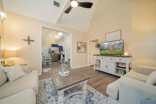 living room featuring high vaulted ceiling, ceiling fan with notable chandelier, wood finished floors, visible vents, and stairway