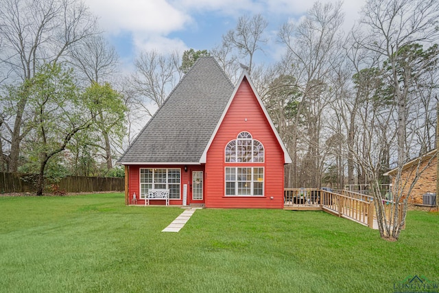 rear view of property featuring a shingled roof, fence, a lawn, and a wooden deck