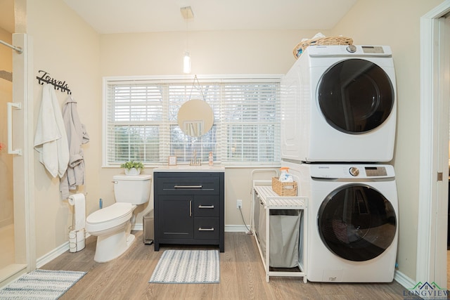 clothes washing area featuring baseboards, light wood-style flooring, and stacked washing maching and dryer