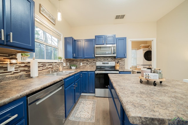 kitchen with blue cabinets, a sink, visible vents, appliances with stainless steel finishes, and stacked washer and clothes dryer