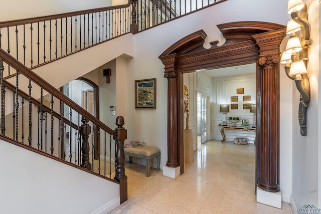 foyer with decorative columns, arched walkways, baseboards, a towering ceiling, and light speckled floor