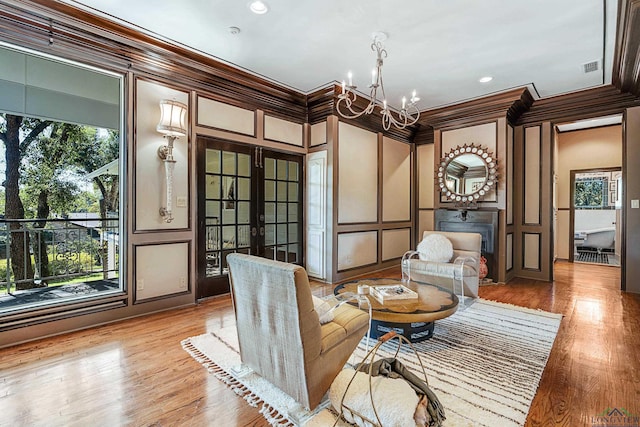 sitting room with light wood finished floors, crown molding, french doors, a chandelier, and a decorative wall