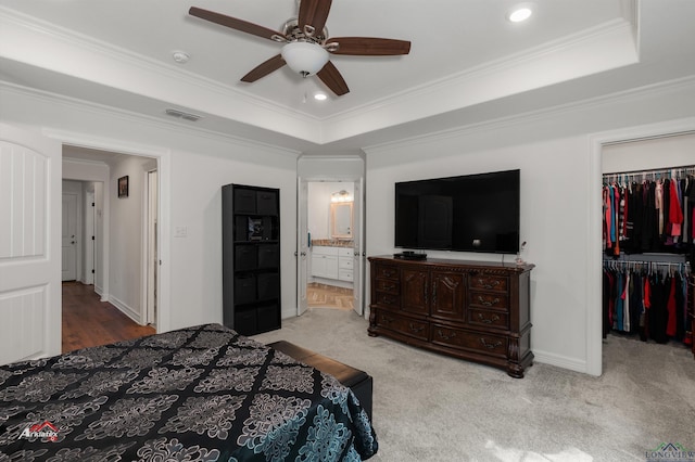 carpeted bedroom featuring ceiling fan, a raised ceiling, ensuite bathroom, a closet, and ornamental molding