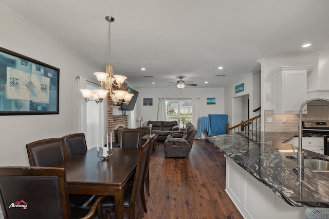 dining room featuring ornamental molding, ceiling fan with notable chandelier, dark wood-type flooring, sink, and a fireplace