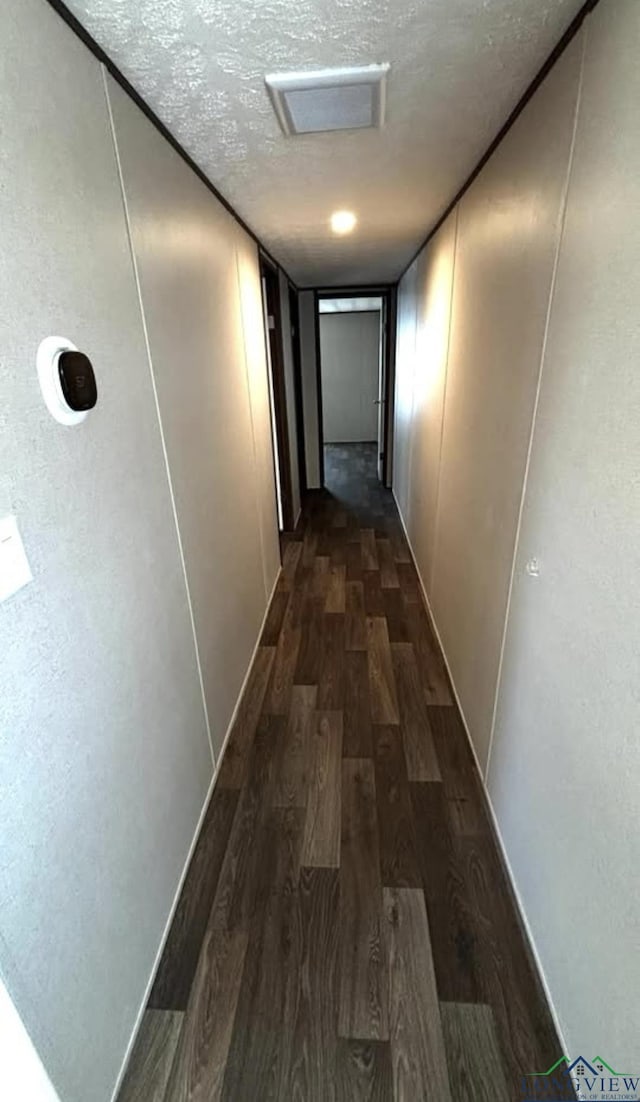 corridor featuring visible vents, a textured ceiling, and dark wood-style flooring