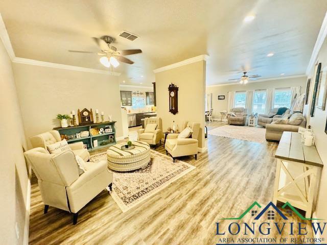 living room featuring a ceiling fan, ornamental molding, visible vents, and wood finished floors