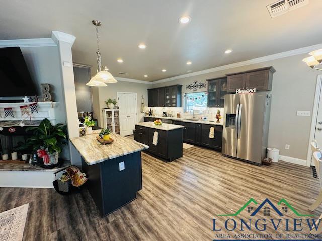 kitchen featuring ornamental molding, visible vents, stainless steel fridge with ice dispenser, glass insert cabinets, and a kitchen island