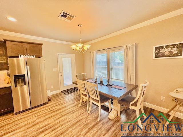 dining area featuring light wood-type flooring, visible vents, baseboards, a chandelier, and ornamental molding