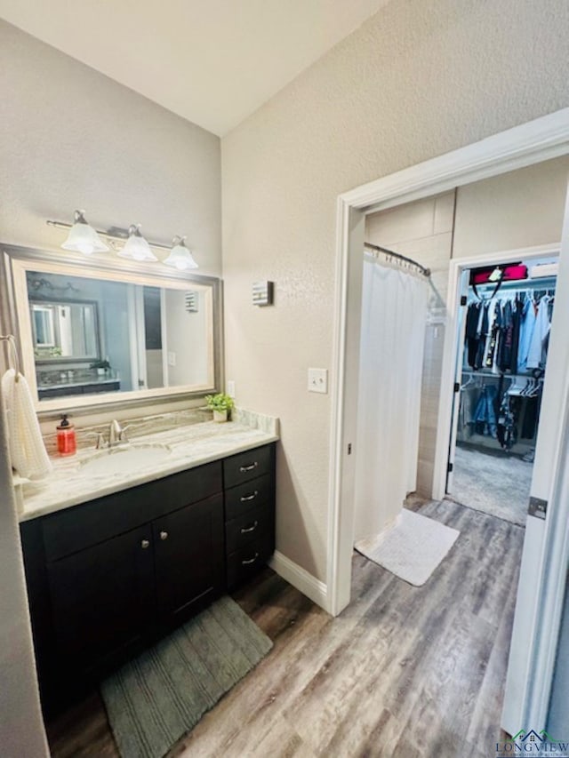 full bath featuring wood finished floors, vanity, curtained shower, a spacious closet, and baseboards
