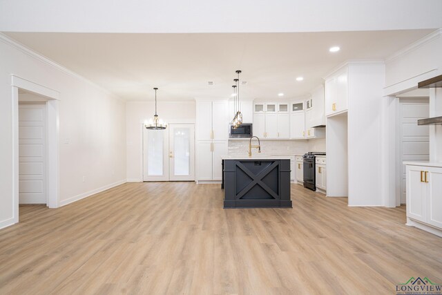 kitchen with built in microwave, decorative light fixtures, an island with sink, white cabinets, and stove