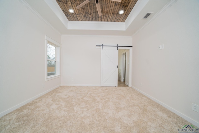 carpeted spare room featuring a barn door, ornamental molding, a tray ceiling, and wooden ceiling