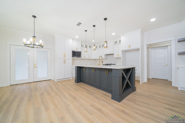 kitchen featuring built in microwave, white cabinetry, a kitchen island with sink, and decorative light fixtures