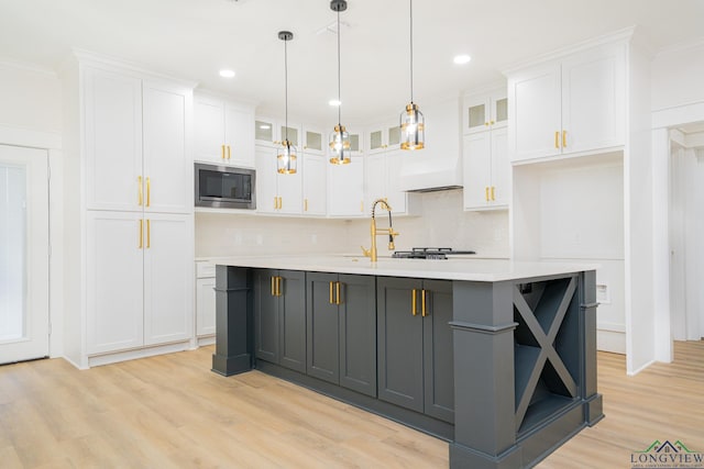 kitchen with a kitchen island with sink, stainless steel microwave, white cabinets, and light wood-type flooring