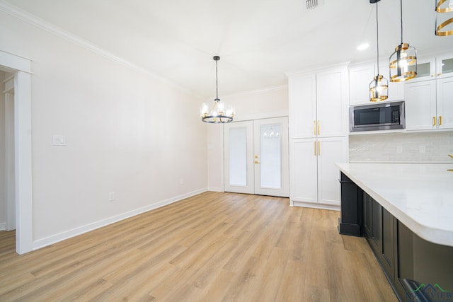 kitchen with stainless steel microwave, decorative light fixtures, white cabinetry, backsplash, and light hardwood / wood-style floors