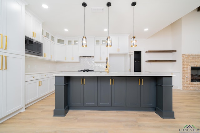 kitchen with built in microwave, white cabinetry, and an island with sink