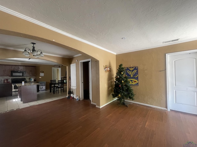 interior space featuring a textured ceiling, light wood-style flooring, visible vents, arched walkways, and an inviting chandelier