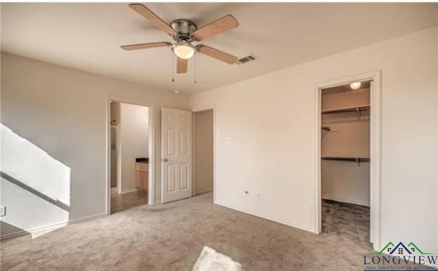 unfurnished bedroom featuring a spacious closet, light colored carpet, a closet, and ceiling fan