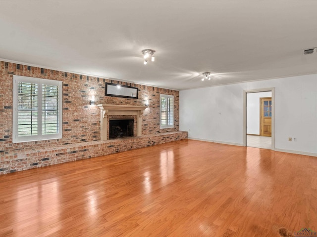 unfurnished living room featuring brick wall, light hardwood / wood-style floors, and a brick fireplace