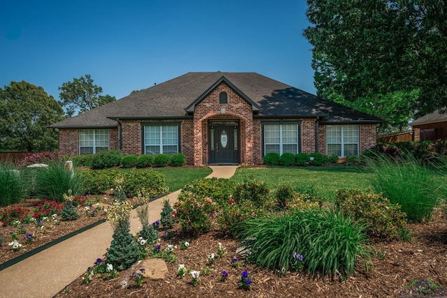 view of front of house with brick siding, a front yard, and roof with shingles