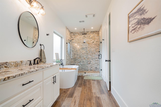 bathroom with a shower stall, wood finished floors, vanity, a freestanding bath, and visible vents