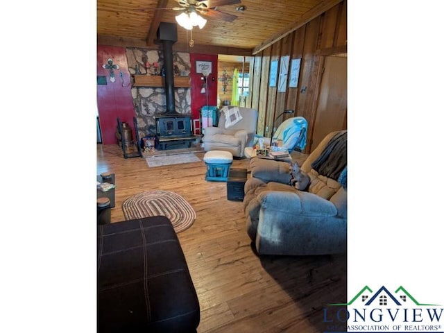 living room with a wood stove, ceiling fan, wood-type flooring, wooden ceiling, and wood walls