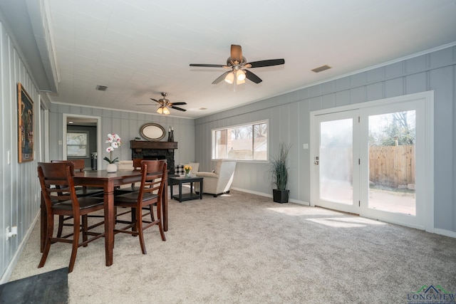 carpeted dining room featuring a fireplace, ceiling fan, and crown molding