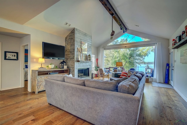 living area featuring baseboards, light wood finished floors, visible vents, a fireplace, and vaulted ceiling with beams