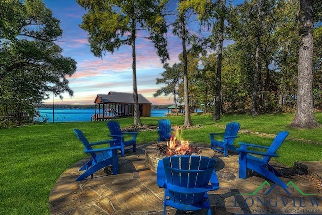patio terrace at dusk with a water view, a fire pit, and a lawn