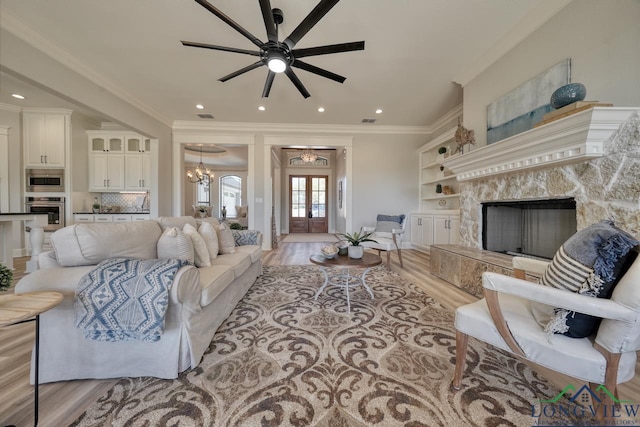 living room featuring ornamental molding, a high end fireplace, ceiling fan with notable chandelier, and light wood-type flooring