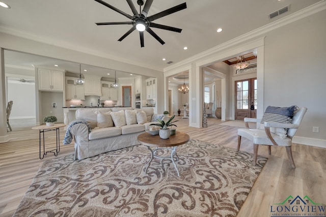 living room featuring ceiling fan with notable chandelier, light hardwood / wood-style flooring, ornamental molding, and french doors