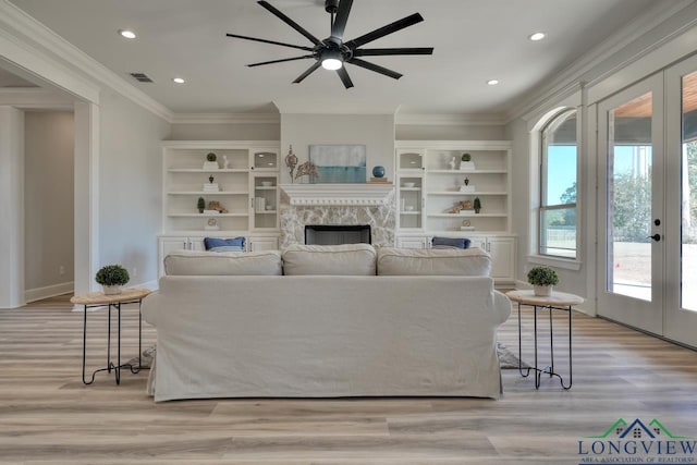 living room with light hardwood / wood-style flooring, crown molding, a fireplace, and french doors