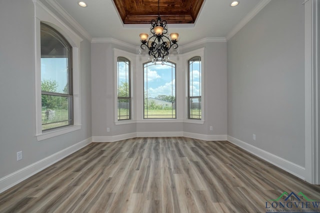 unfurnished room featuring hardwood / wood-style flooring, ornamental molding, a raised ceiling, and a notable chandelier