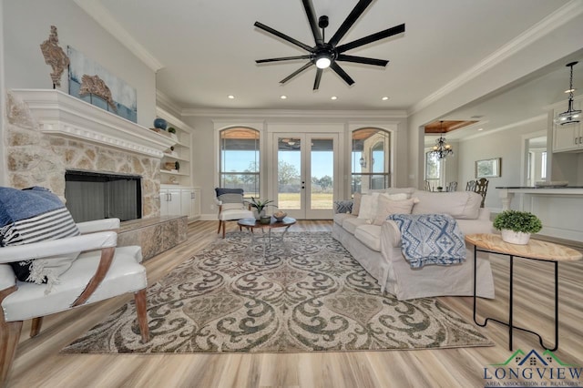 living room featuring built in features, a fireplace, ornamental molding, french doors, and light wood-type flooring